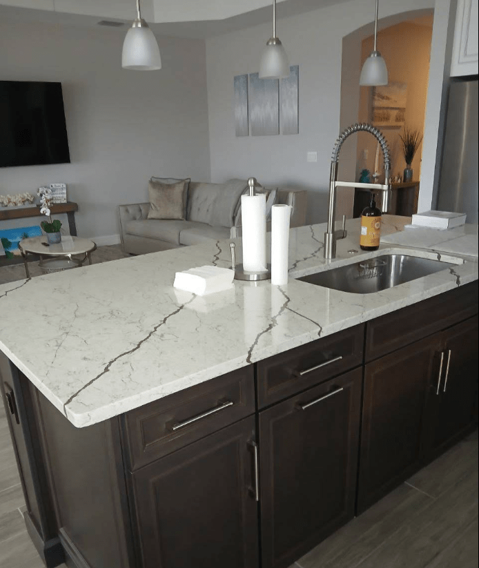 Modern kitchen countertop with dark cabinetry, featuring a marble surface, sink, and decorative items, set in an open living space.