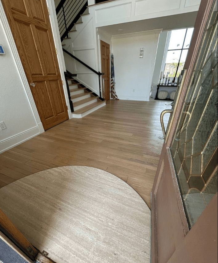 Spacious foyer with wooden flooring, a staircase on the left, and an entry door featuring glass panel details, creating a warm entrance.