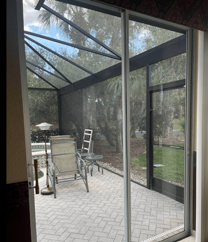 A view through a large sliding glass door shows a well-lit interior with a ceiling fan and a kitchen area.