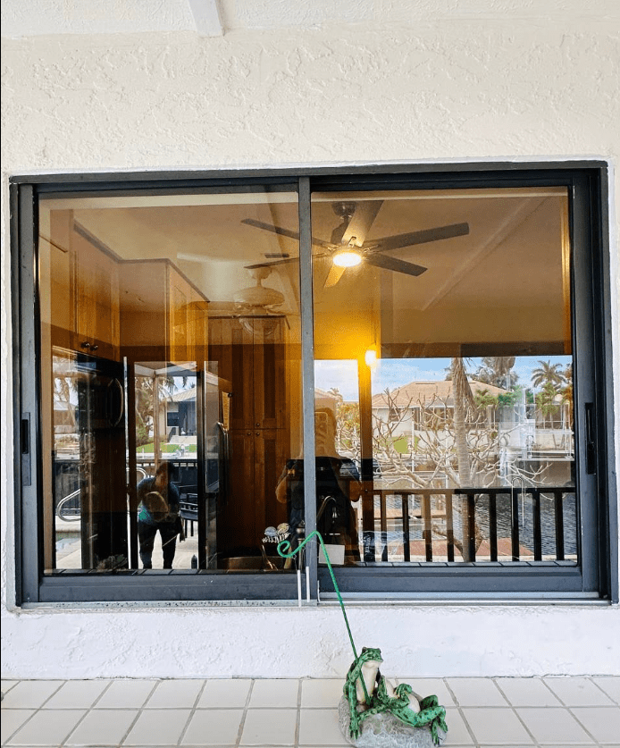A view through a large sliding glass door shows a well-lit interior with a ceiling fan and a kitchen area, alongside a patio with a decorative frog.