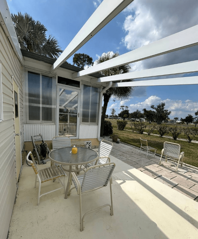 Bright patio featuring a round glass table and six chairs, surrounded by palms. Ideal for outdoor gatherings, with a clear sky enhancing the ambiance.