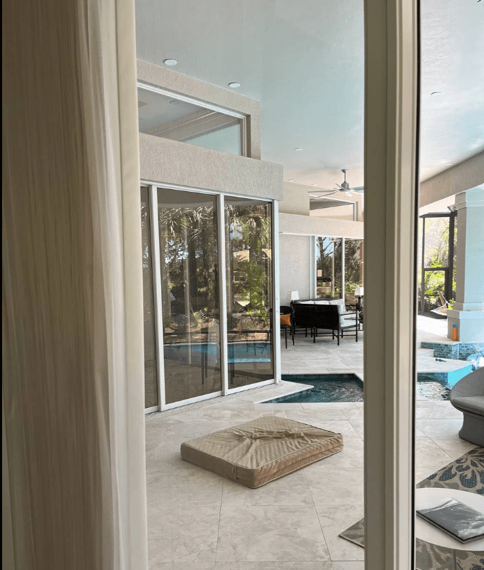 Bright indoor space showcasing a modern patio with a seating area and a view of a pool. A pet bed is placed on the tiled floor, suggesting pet-friendly design.
